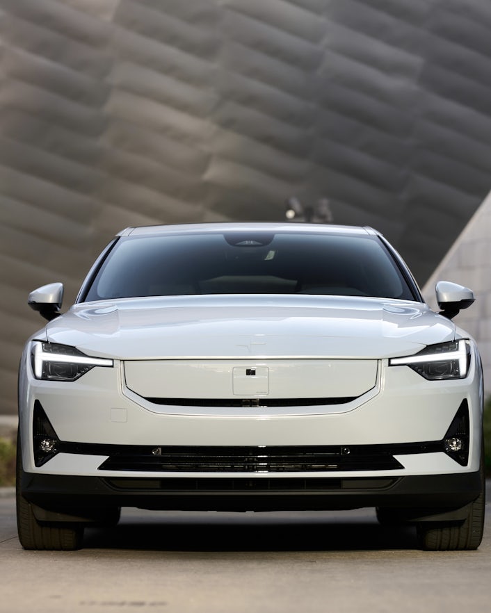 Front view of a pristine white Polestar 2 parked in front of a tall building.