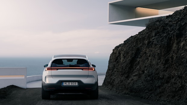 A snow white Polestar 3 parked on a road with the ocean in the background.