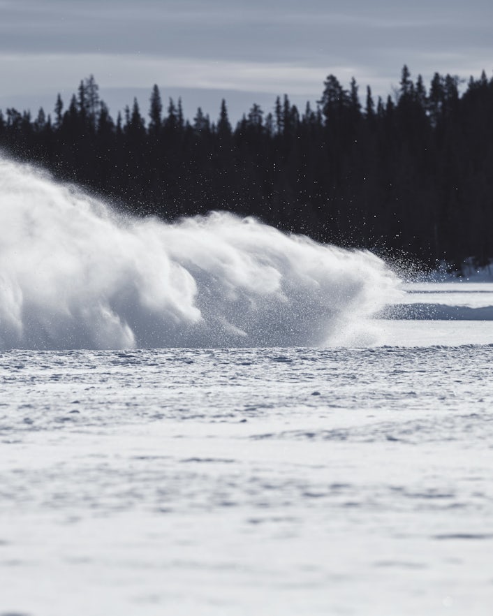 A big cloud of snow sweeps across a snow-filled landscape.