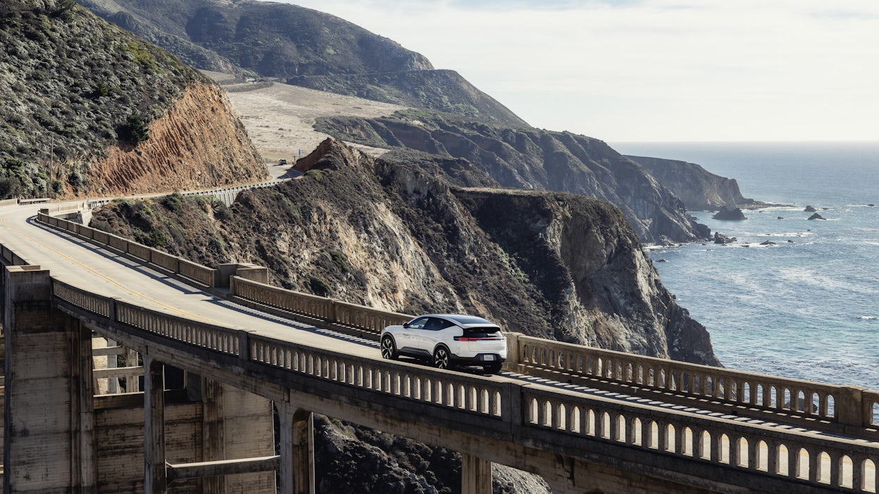 Polestar 3 from afar driving over a bridge overlooking the ocean.