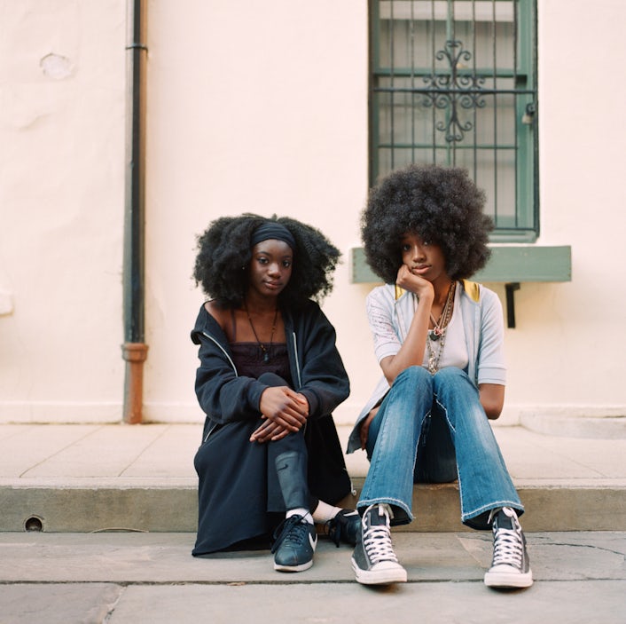 Two people sitting on the sidewalk looking into the camera.