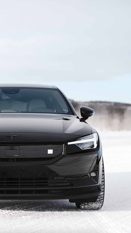 Black Polestar 2 driving on ice in a winter landscape snow blowing behind the car