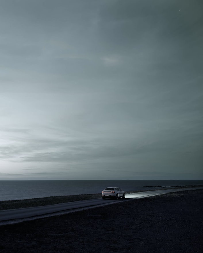 Polestar 2 in distance driving at night next to sea