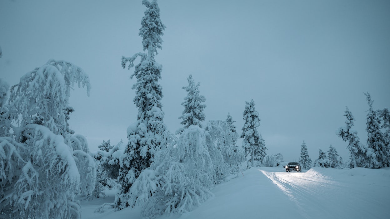 Polestar 2 driving on a snowy road in Levi, surrounded by forest.