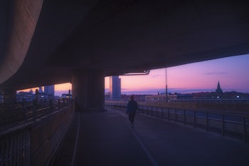 A person walking under a bridge at sunrise.