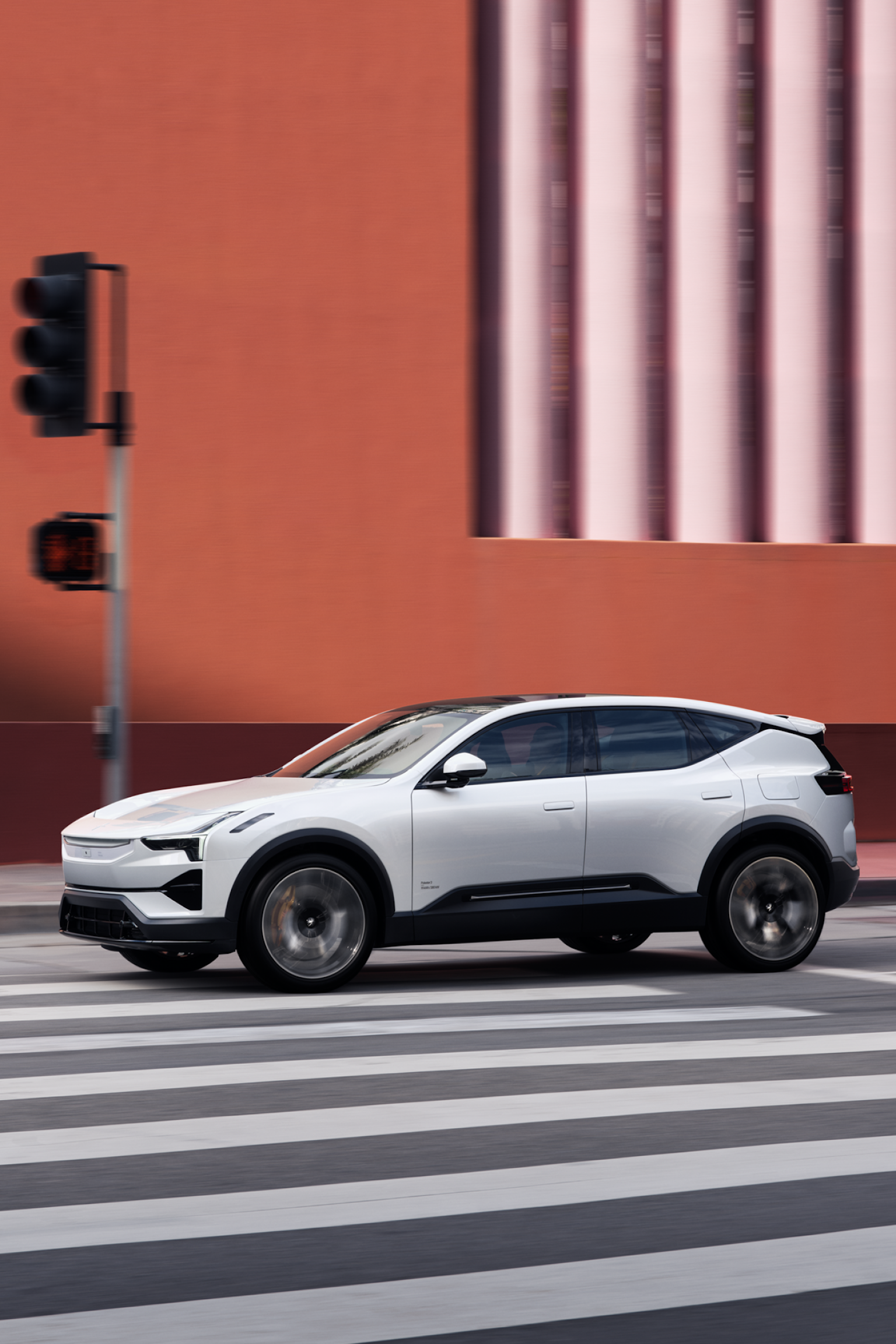 Polestar 3 driving on a road with zebra crossing past a red building.