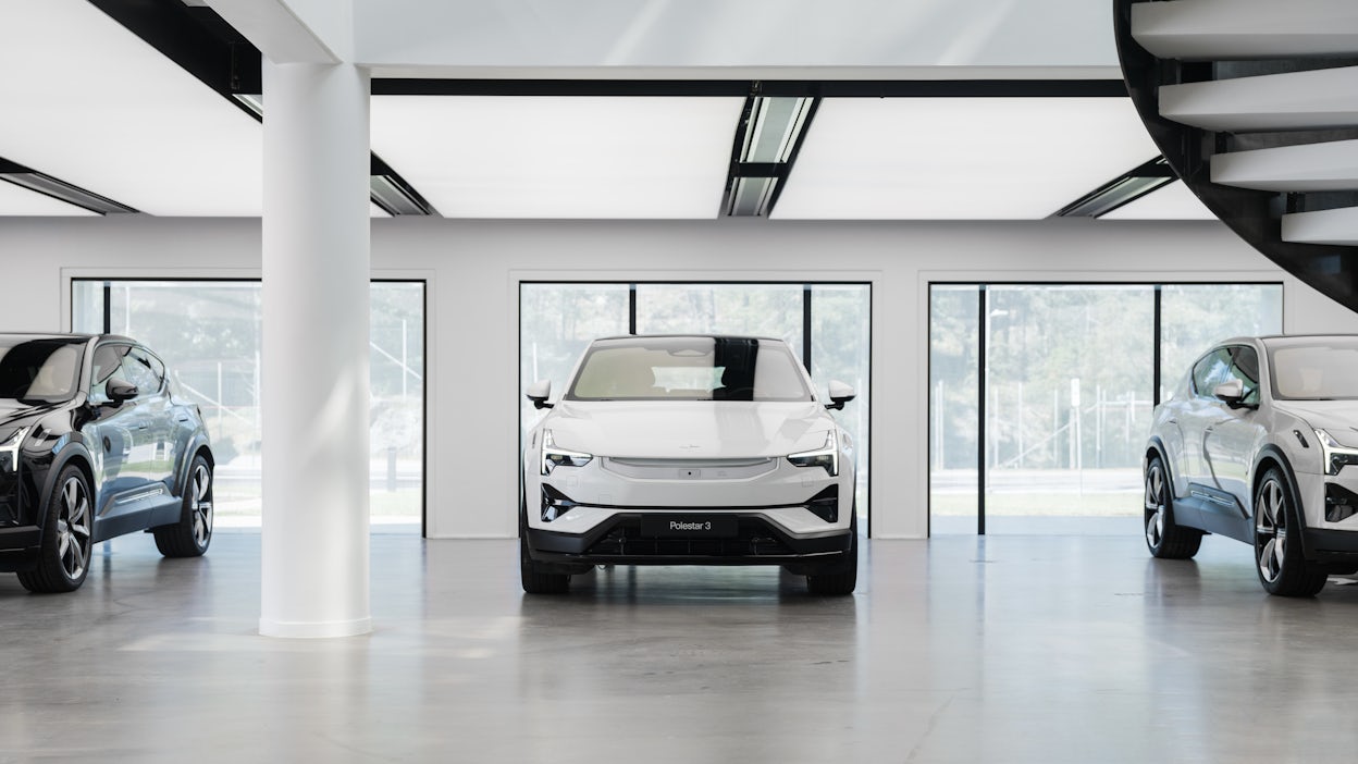 Polestar cars displayed indoors with large windows and a spiral staircase visible on the right.