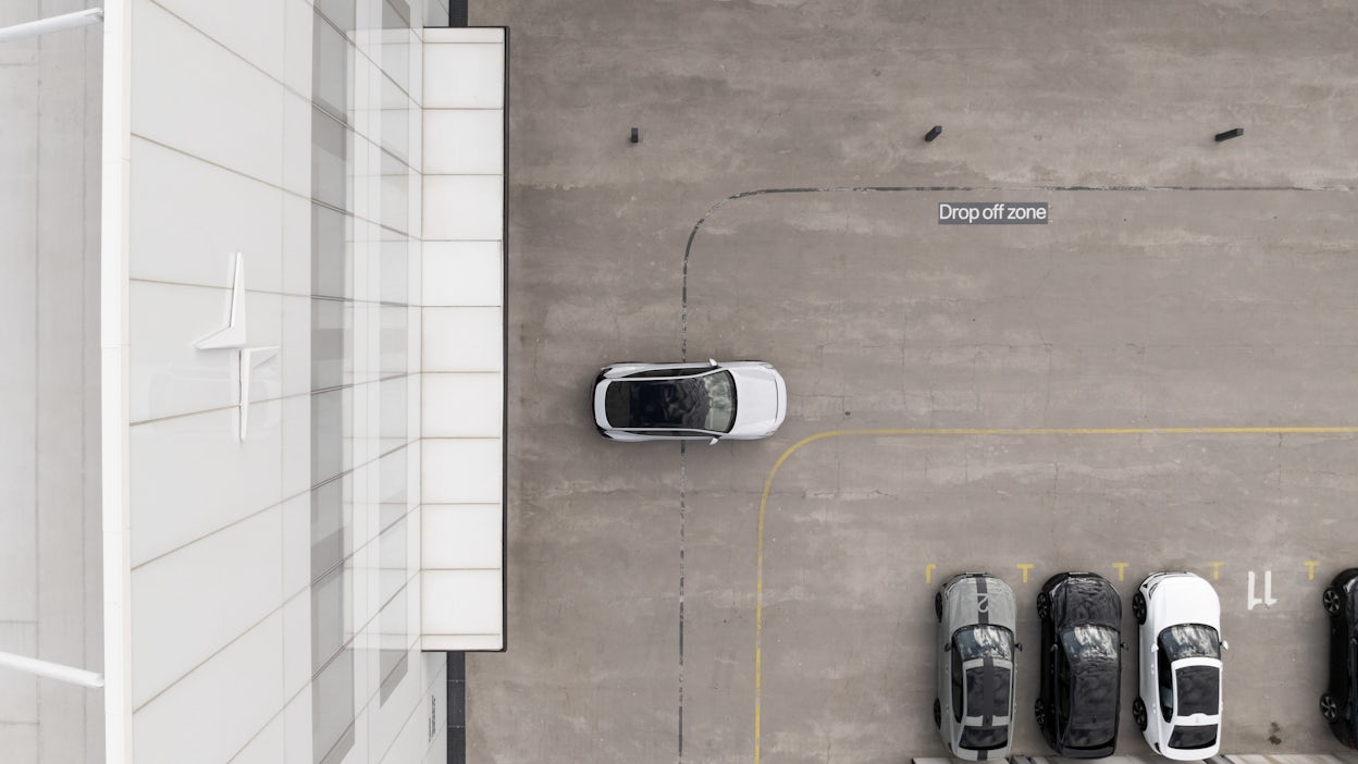 Polestar car parked in drop-off zone near building with Polestar logo, adjacent to other parked cars.