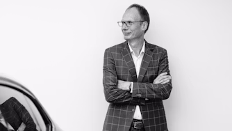 Person in checkered suit standing with arms crossed near Polestar car.