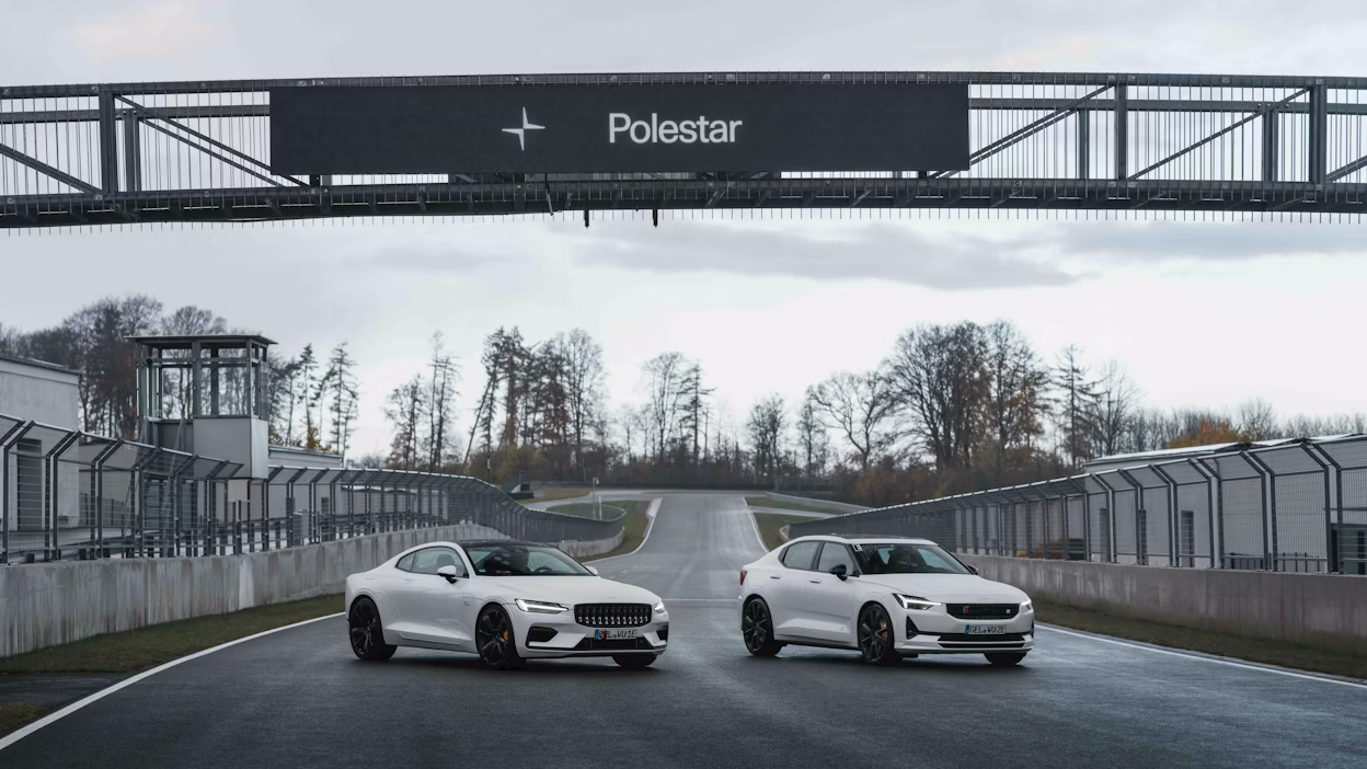 Two Polestar cars on a racetrack under a Polestar sign with trees and fencing in the background.