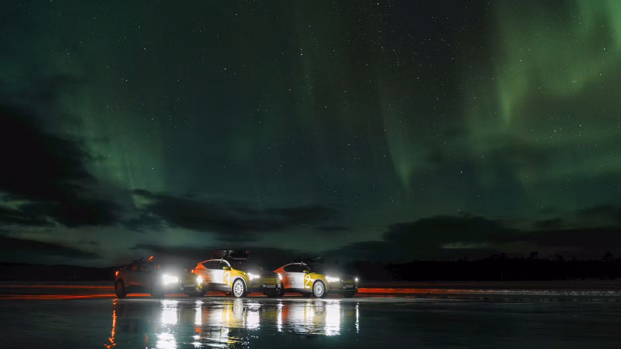 Three white and yellow cars parked on a frozen lake under Northern Lights