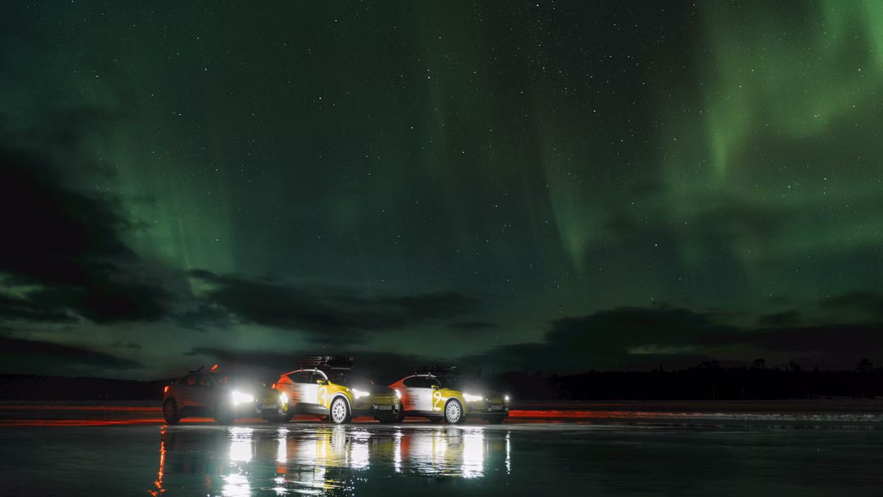 Three white and yellow cars parked on a frozen lake under Northern Lights