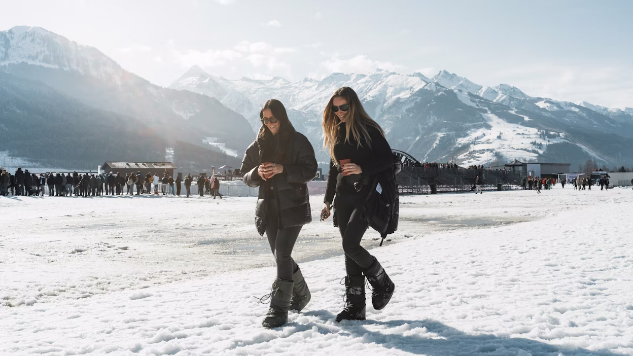 Two women walk in front of snowy mountain range