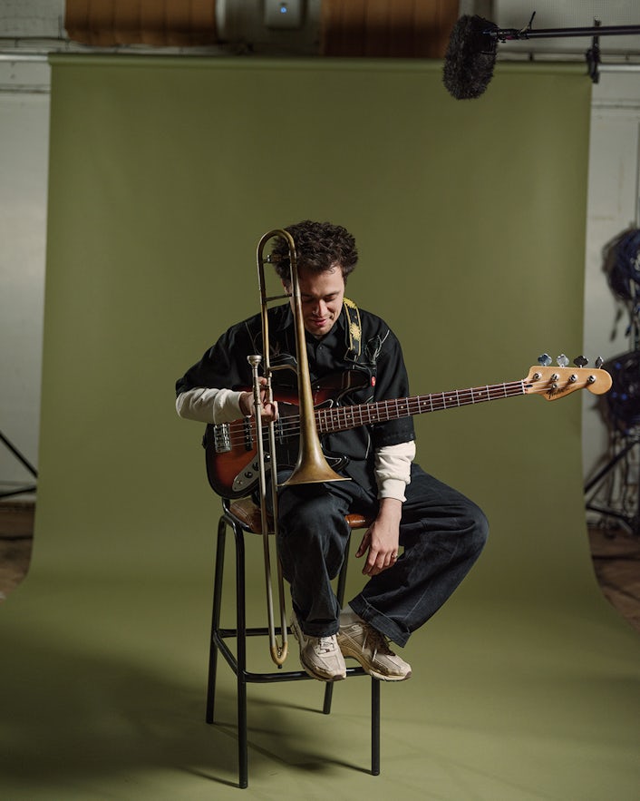 Man sitting on stool holding guitar and trombone
