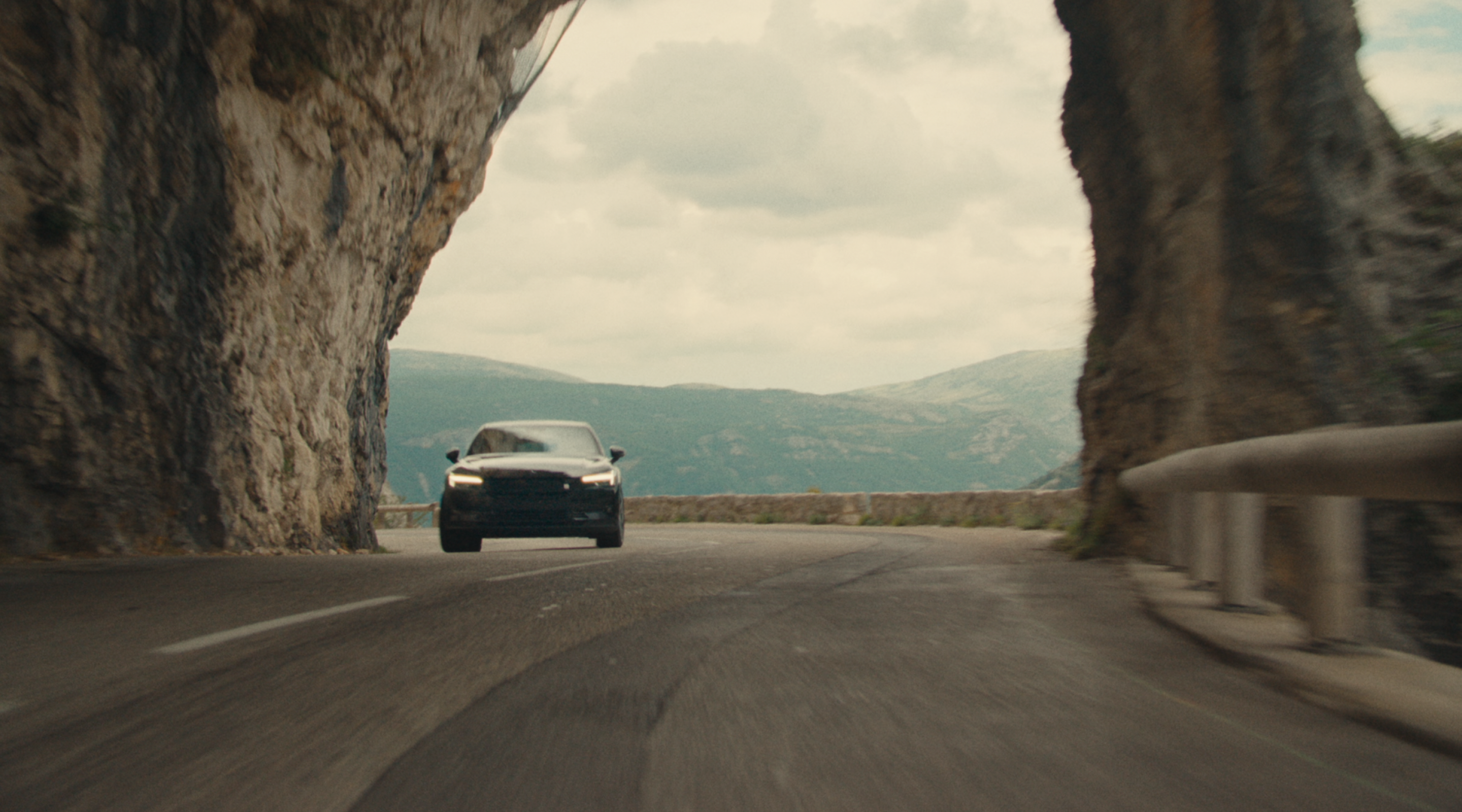 Polestar 2 driving through narrow streets and on a motorway by the side of a mountain.