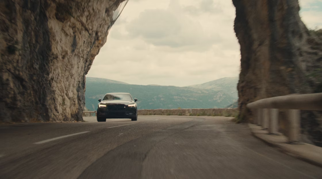 Polestar 2 driving through narrow streets and on a motorway by the side of a mountain.