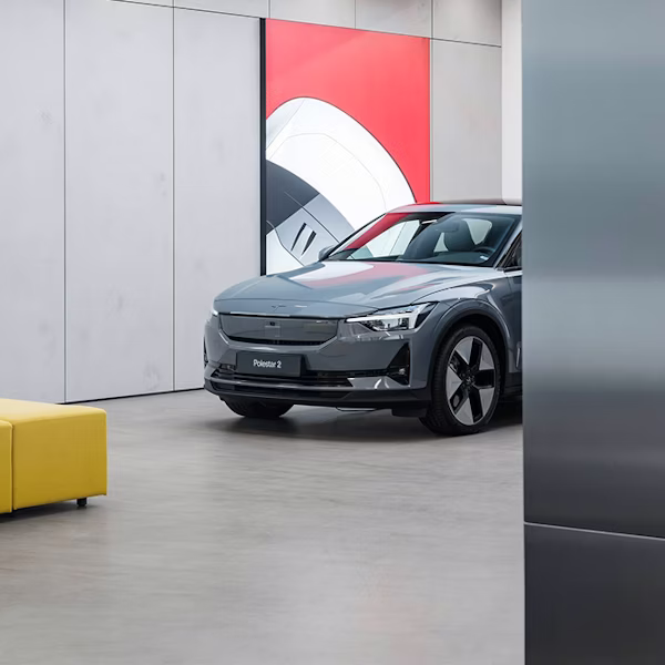 Polestar 2 car parked indoors in a Space near a yellow sofa and a wall with red and white artwork.