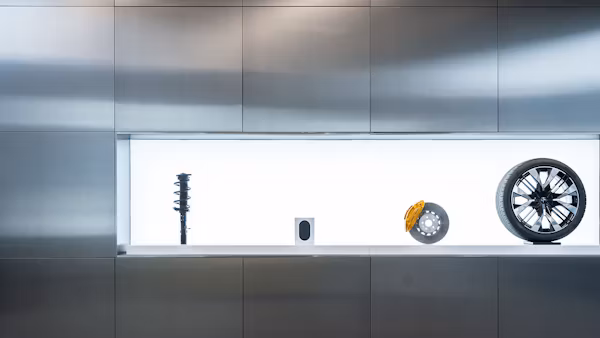 Display of car suspension, speaker, brake disc with caliper, and wheel against a metallic wall.