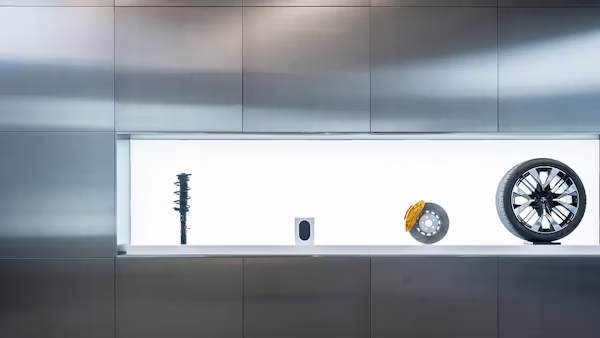 Display of car suspension, speaker, brake disc with caliper, and wheel against a metallic wall.