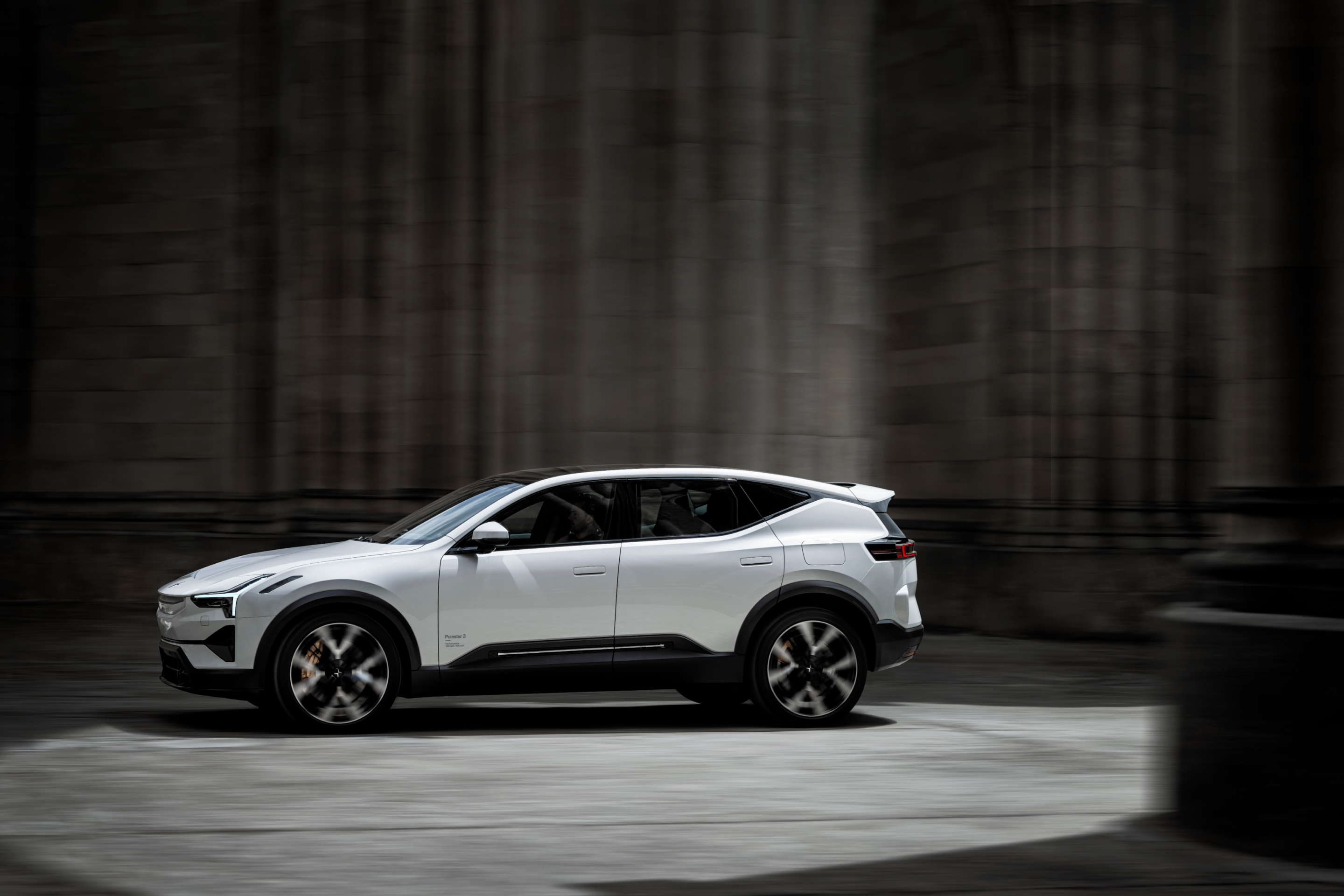 A white Polestar 3 driving between grey stone columns and walls.