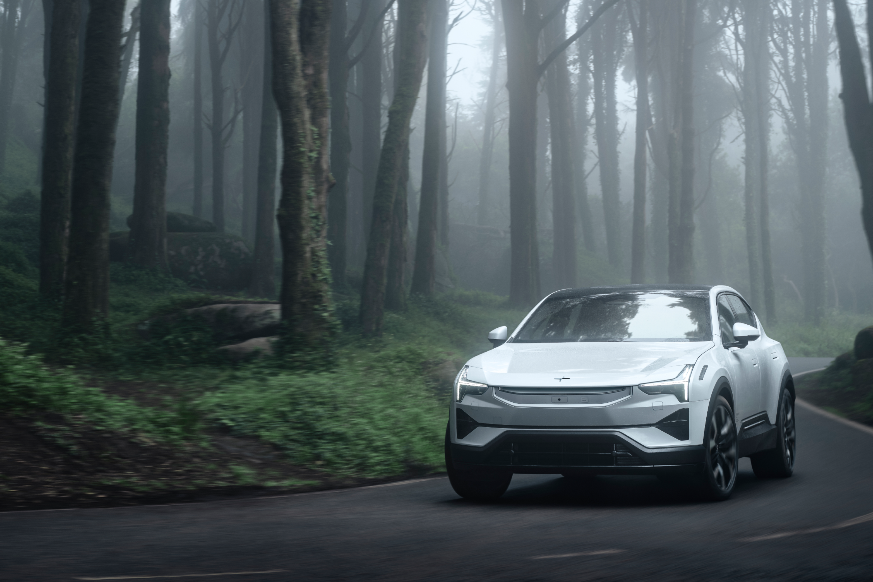 A white Polestar 3 driving on a road in a foggy environment with trees and green foliage.