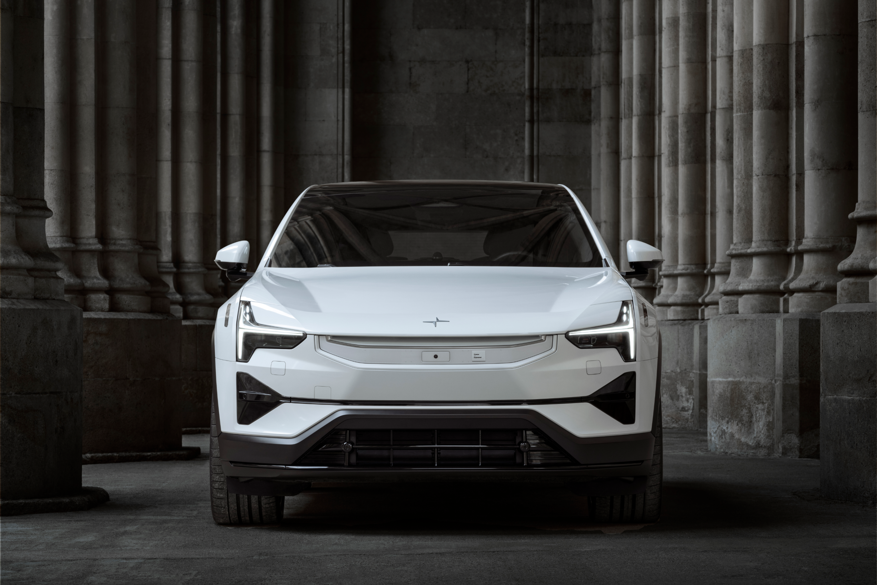A portrait view of a white Polestar 3 standing between grey stone columns and walls.