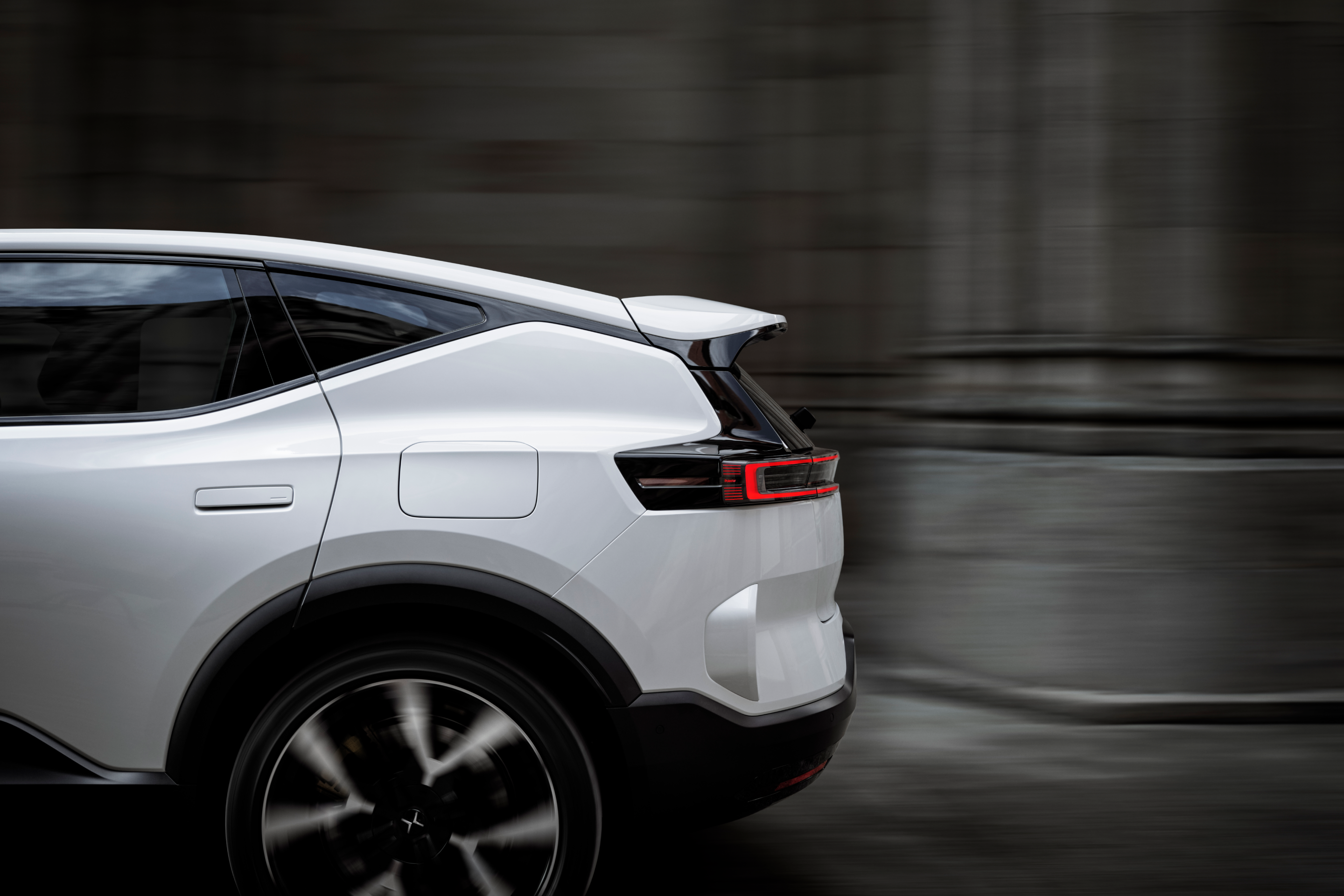A side view of the back half of a white Polestar 3 driving by grey stone walls and columns.