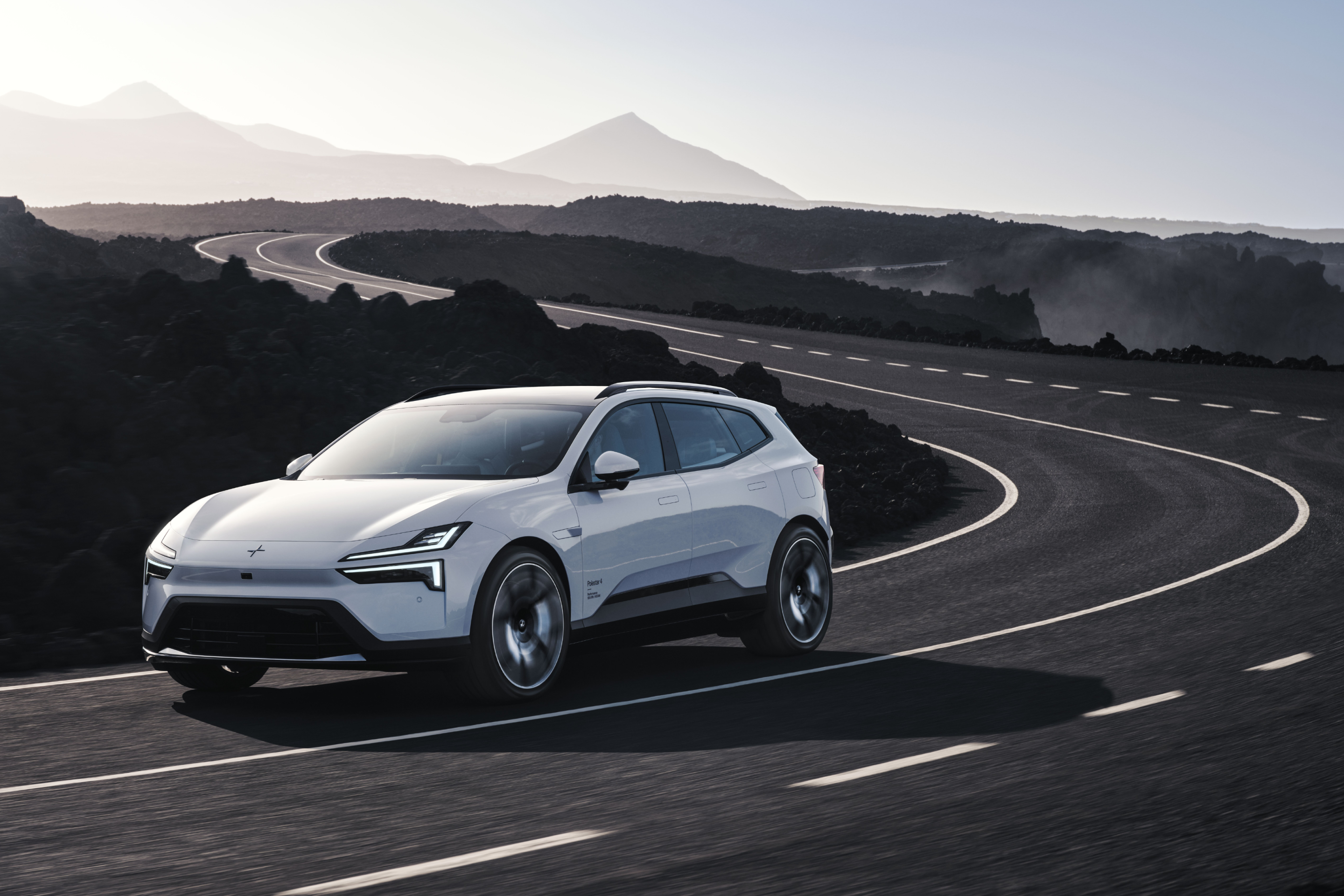 White Polestar 4 SUV driving on a grey road with hazy mountains in the background.