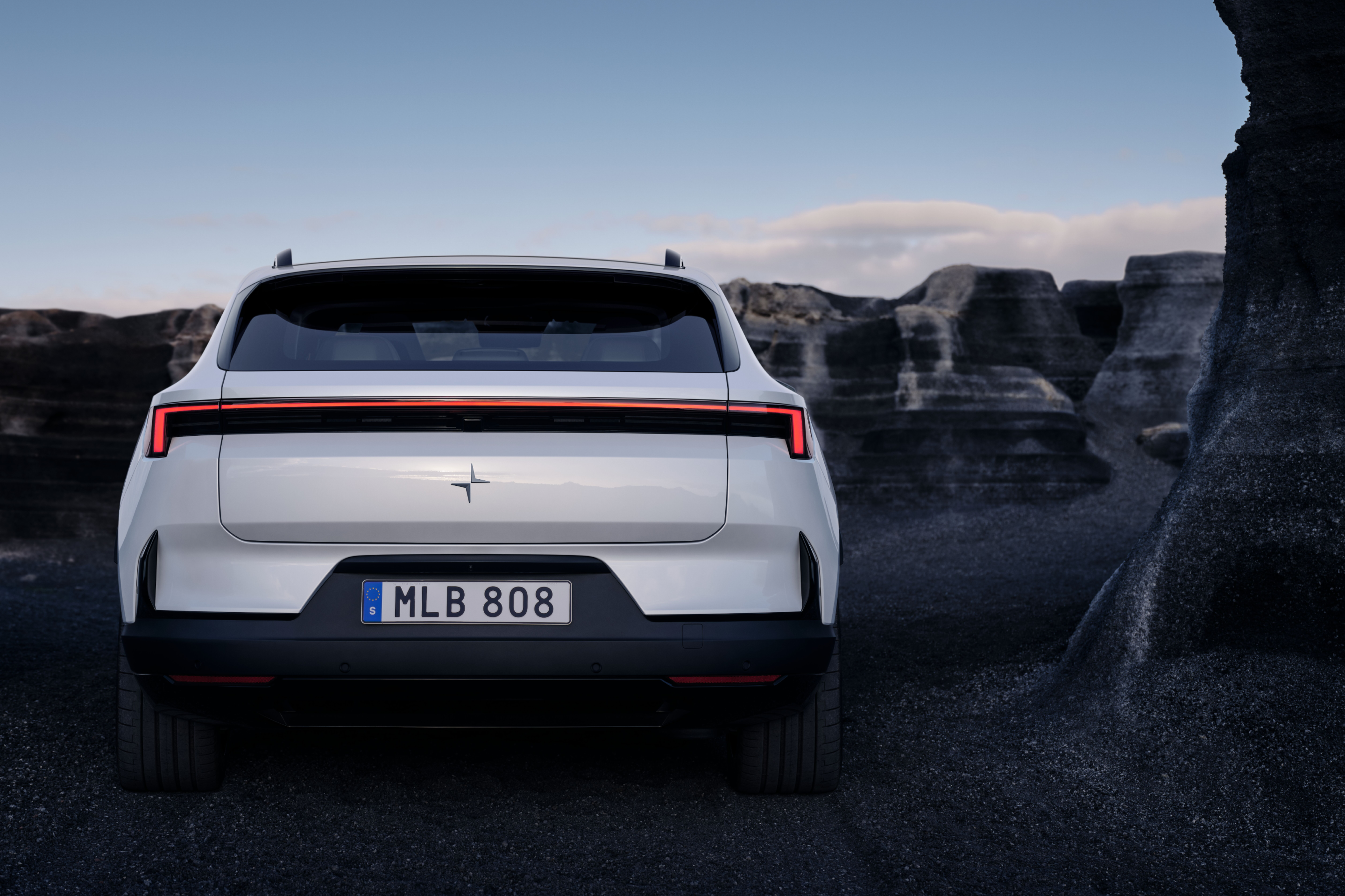 Rear profile view of a white Polestar 4 SUV standing against beside seaside cliffs.