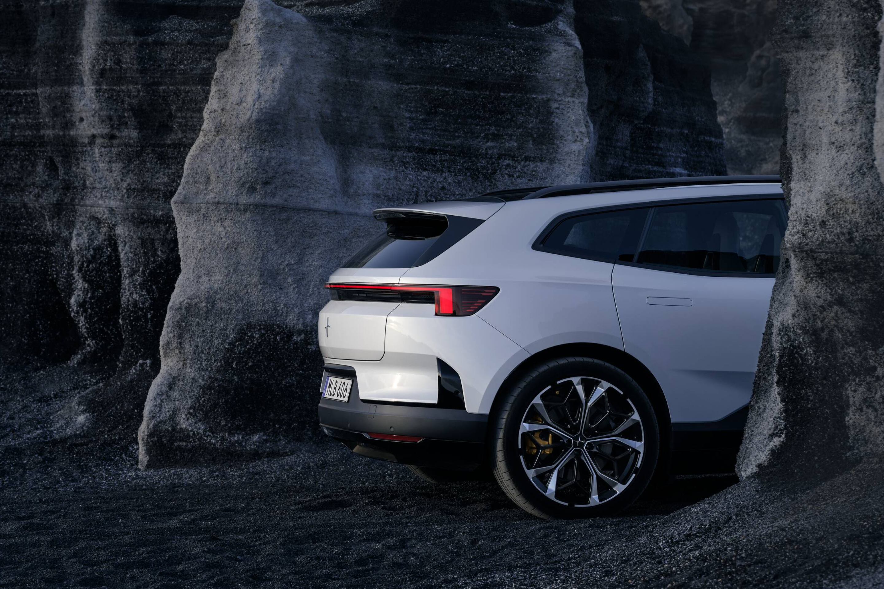 Rear side portion of a white Polestar 4 SUV standing between a grey rock formation.
